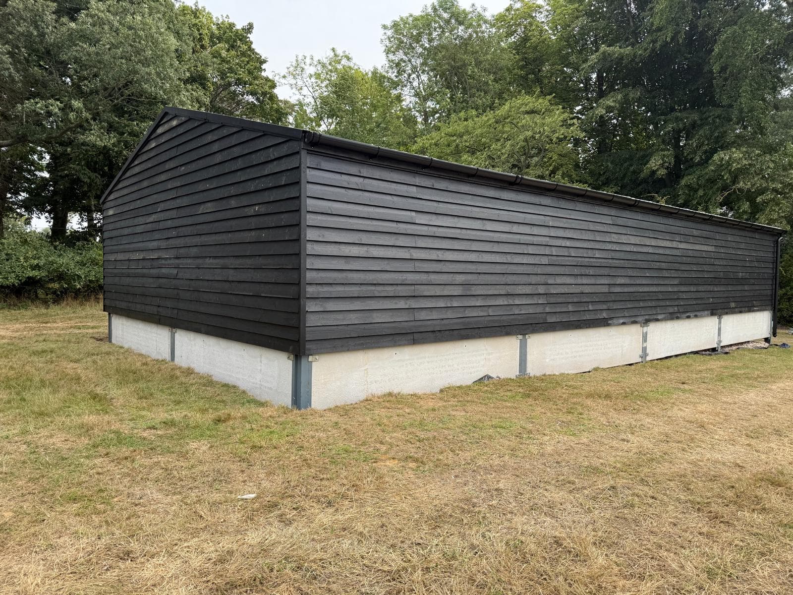 Completed black-clad agricultural building with side elevation across a rural setting